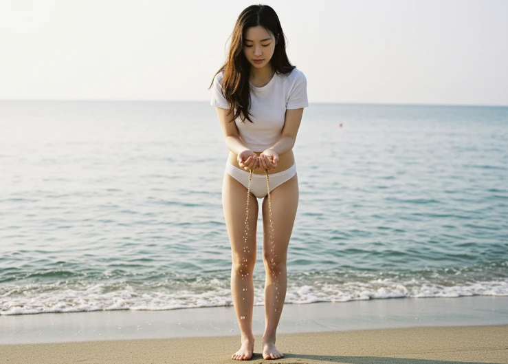 바닷가에서 손바닥 위 모래알이 물에 씻겨 내려가는 모습을 바라보는 한국 여성
